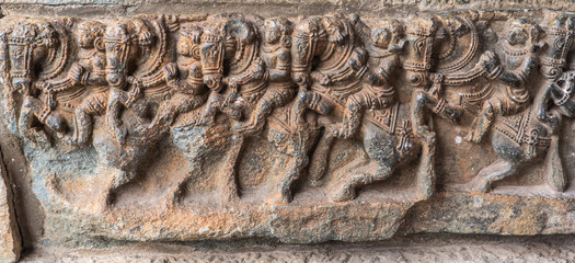 Belur, Karnataka, India - November 2, 2013: Brown stone plinth sculpture of row of horses with warriors riding them at bottom of Chennakeshava Temple building.