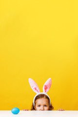 Fototapeta premium Cute little child girl with bunny ears at home is hunting for Easter eggs.