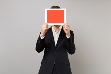 Young business man in classic suit hiding and covering face with tablet pc computer with blank empty screen isolated on grey background. Achievement career wealth business concept. Mock up copy space.