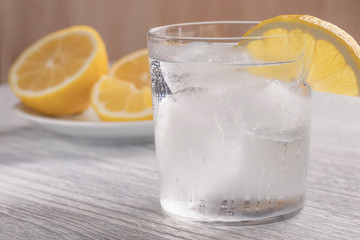 Refreshing cold water with lemon. With ice. Ready to eat. Next is a knife after cutting fruit. Misted glass.