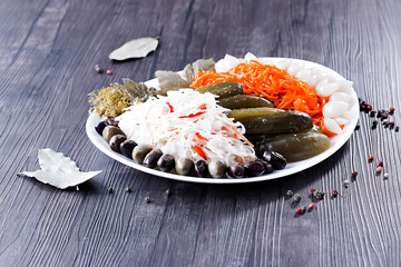 Assorted pickled and fermented vegetables in a white plate on a brown wooden background.