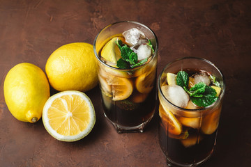 Cuba Libre cocktail with rum, cola, mint, lemon and ice in the glass on a brown background