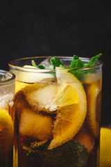 Cuba Libre cocktail with rum, cola, mint, lemon and ice in the glass on a brown table and black background
