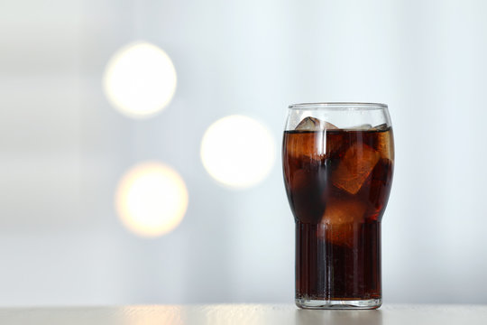 Glass of cola with ice on table against blurred background. Space for text
