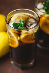 Cuba Libre cocktail with rum, cola, mint, lemon and ice in the glass on a brown background