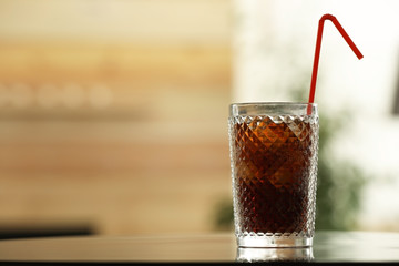 Glass of cola with ice on table against blurred background. Space for text