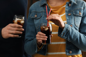 People holding glasses of cola with ice on blurred background, closeup