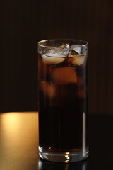 Glass of cola with ice on table against blurred background
