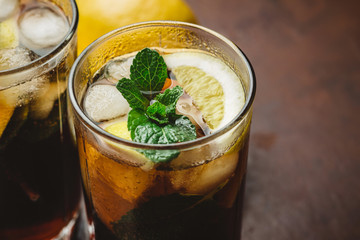 Cuba Libre cocktail with rum, cola, mint, lemon and ice in the glass on a brown background