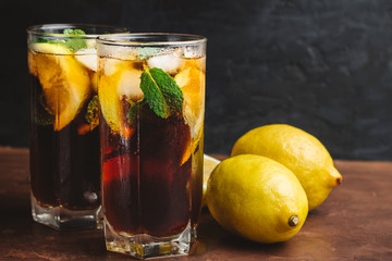 Cuba Libre cocktail with rum, cola, mint, lemon and ice in the glass on a brown table and black background