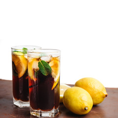 Cuba Libre cocktail with rum, cola, mint, lemon and ice in the glass on a brown table and white background