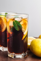 Cuba Libre cocktail with rum, cola, mint, lemon and ice in the glass on a brown table