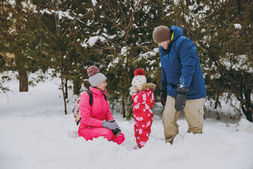 Funny family woman, man and little girl in winter warm clothes playing, having fun in snowy park or forest outdoors. Winter fun, leisure on holidays. Love relationship family people lifestyle concept.