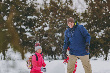 Cheerful family woman, man and little girl in winter warm clothes playing, making snowman in snowy park or forest outdoors. Winter fun, leisure on holidays. Love relationship family lifestyle concept.