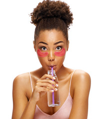 Young girl with pink eye patches on her face and drinks clean water. Photo of african american girl isolated on white background. Youth and Beauty