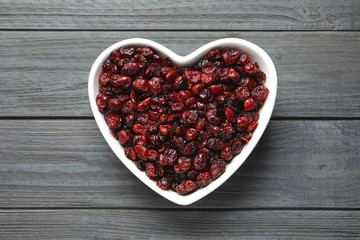 Heart shaped bowl with cranberries on wooden background, top view. Dried fruit as healthy snack