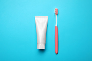 Blank tube of toothpaste and brush on color background, top view