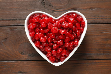 Heart shaped bowl of sweet cherries on wooden background, top view. Dried fruit as healthy snack