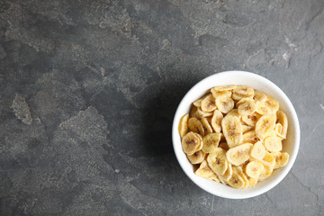 Bowl with sweet banana slices on grey background, top view with space for text. Dried fruit as healthy snack