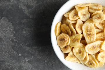 Bowl with sweet banana slices on grey background, top view with space for text. Dried fruit as healthy snack