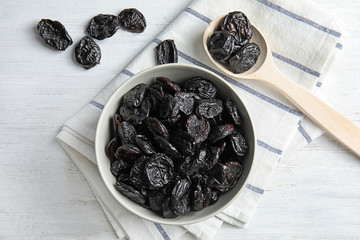 Bowl and spoon of sweet dried plums on table, top view. Healthy fruit