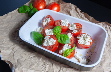 Fresh vegetarian sliced and salted tomatoes ready to bake covered with cheese and fresh organic basil