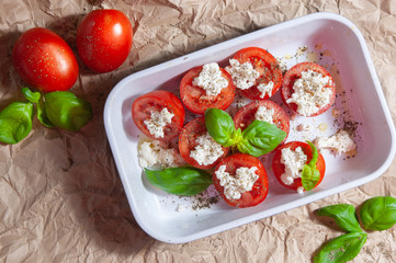 Fresh vegetarian sliced and salted tomatoes ready to bake covered with cheese and fresh organic basil