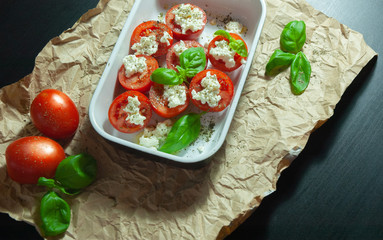 Fresh vegetarian sliced and salted tomatoes ready to bake covered with cheese and fresh organic basil