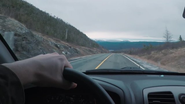 Driving POV on top of a mountains peak. The window view is larger mountains in the distance.