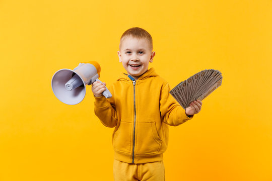 Little happy kid boy in yellow clothes hold fan of money in dollar banknotes, megaphone isolated on orange wall background, children studio portrait. Childhood lifestyle concept. Mock up copy space.