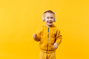 Little kid boy 3-4 years old wearing yellow clothes in headphones isolated on orange wall background, children studio portrait. People sincere emotions, childhood lifestyle concept. Mock up copy space