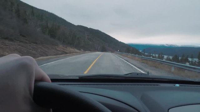 Driving POV on top of a mountains peak. The window view is larger mountains in the distance.