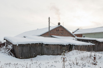 House in a Russian village in the winter, in the snow, with old shabby wooden barns in the foreground