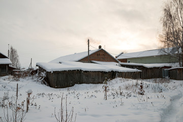 House in a Russian village in the winter, in the snow, with old shabby wooden barns in the foreground