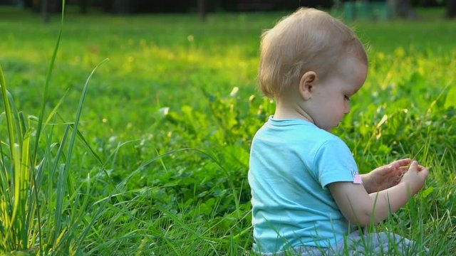 Happy baby boy sitting on the grass in the park, slow motion