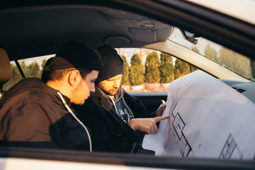 Two robbers planning and pointing on the blueprint(map) their objective while holding their guns.