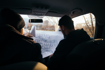 Two violent robbers sitting in a car looking at a blueprint of the building they want to rob while...