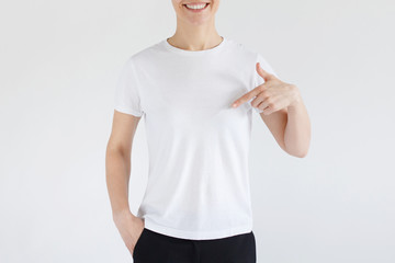Young woman smiling while pointing with index finger to white t-shirt, copyspace for advertising, isolated on gray background. No face photo