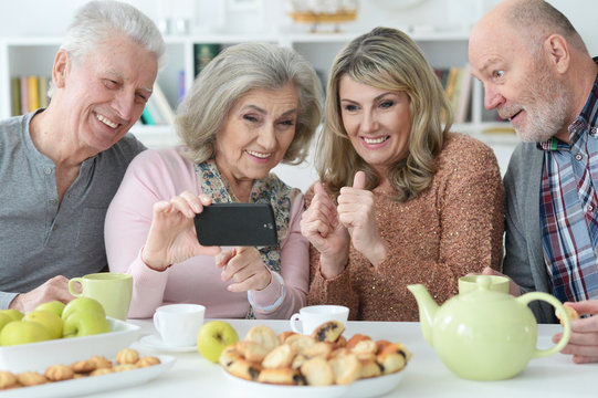 two Senior couples using smartphone during morning tea