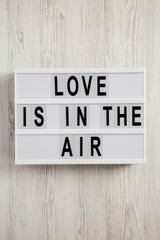 Modern board with text 'Love is in the air' on a white wooden background. Valentine's Day 14 February.