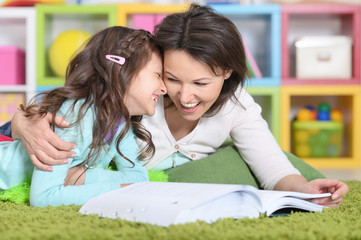 mother with  daughter reading book while lying on floor