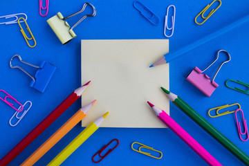 Top view of the empty blank  for writing, color pencils and clips  on the blue background.Copy space.