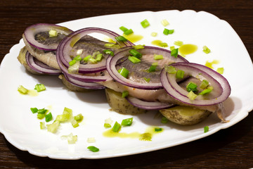 herring with boiled potatoes and fresh onions on a plate, close-up