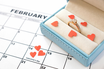 Valentine's day, February 14 on the calendar with red hearts and wedding ring in blue box. Offer to marry