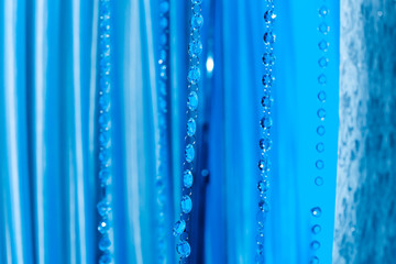 Fototapeta na wymiar many chains with transparent pebbles on a background of blue tulle