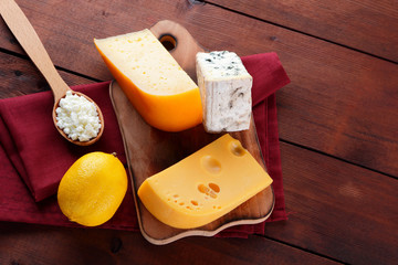 Hard cheese, blue cheese and cottage cheese on a wooden board. Different types of cheese on a red napkin. Dairy products and lemon on a wooden background. Top view
