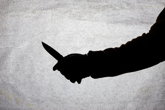 The knife in the hand of men who is ready to attack his victim. Breaking the law and crime. Attack with a knife. Silhouette on a light background.