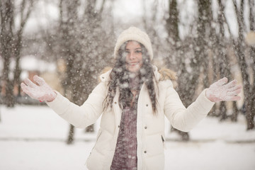 Young beautiful woman is enjoying the snow scattering it in the air, positive emotions, joy and happiness. Winter outdoor activities