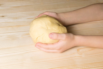Dough in the hands of a child on a wooden background. Homemade dough for bread, pasta, dumplings, ravioli. Home kitchen.