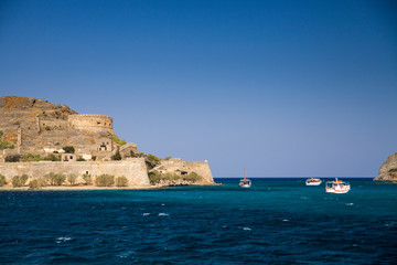 Fototapeta na wymiar Cruise to the island of Spinalonga. Small boat on the blue lagoon. Spinalonga fortress on the island of Crete, Greece. Architecture on the island.